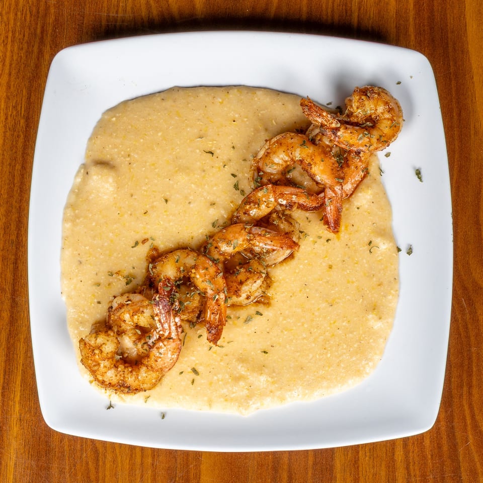Melvin's at Riverside's shrimp and grits, a southern dish, on a white plate.