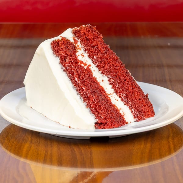 A slice of Melvin's at Riverside's red velvet cake with white frosting on a white plate.
