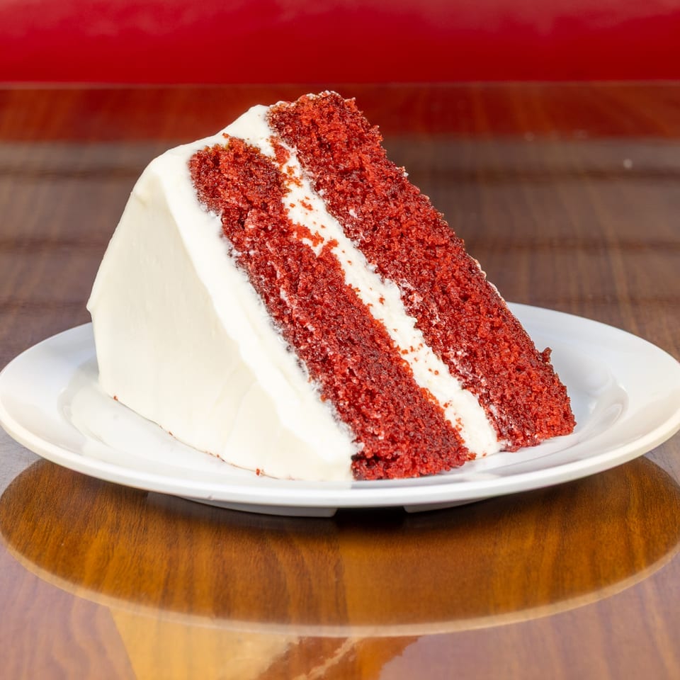 A slice of Melvin's at Riverside's red velvet cake with white frosting on a white plate.