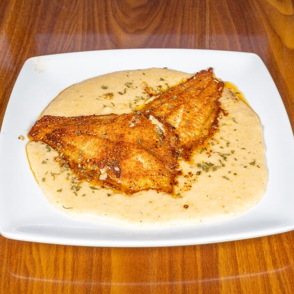 Southern-style fish and grits, featuring a seasoned fillet atop creamy grits, garnished with herbs.