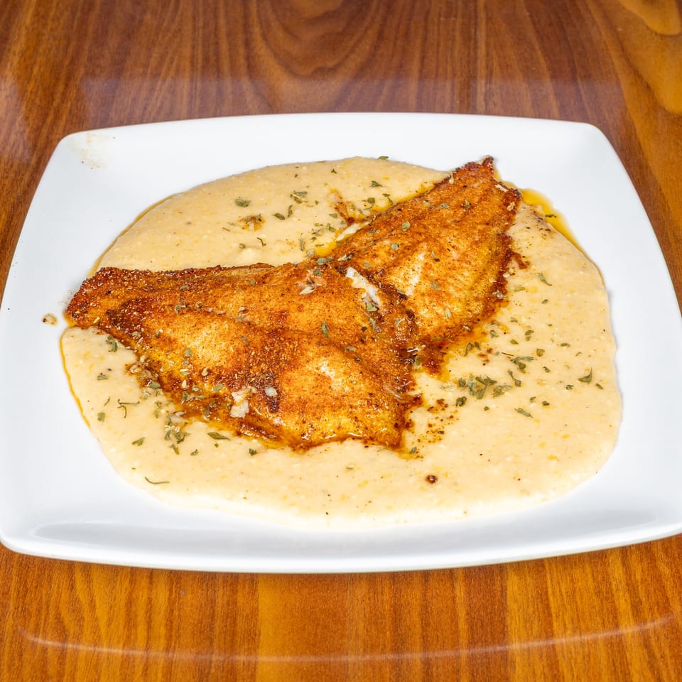 Southern-style fish and grits, featuring a seasoned fillet atop creamy grits, garnished with herbs.