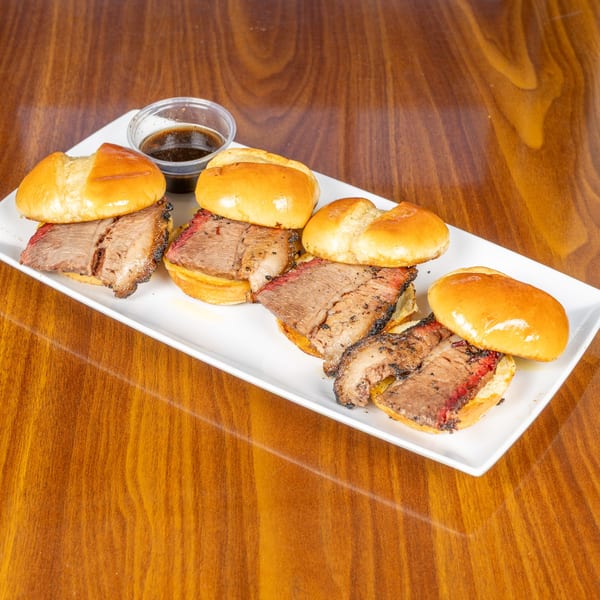 Four southern brisket sliders on a white plate with a side of barbecue sauce on a wooden table.