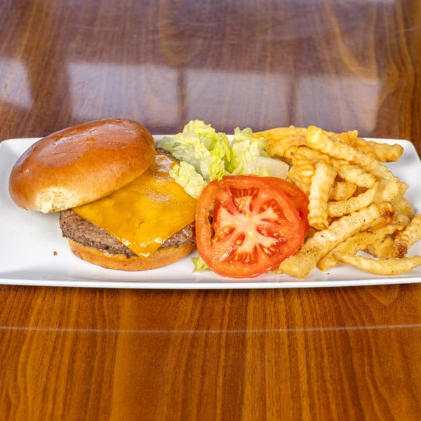 Cheeseburger with melted cheese, lettuce, tomato slices, and crinkle-cut fries on a white plate.