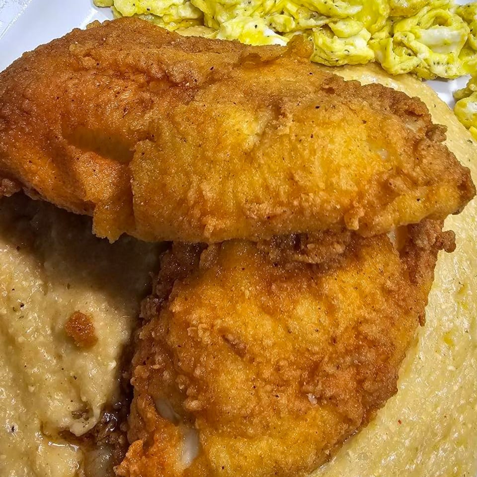 Golden fried fish fillets with creamy grits and scrambled eggs on a white plate.