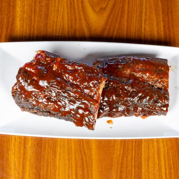 Two racks of Melvin's at Riverside's southern-style BBQ ribs, glistening with sauce on a white plate.