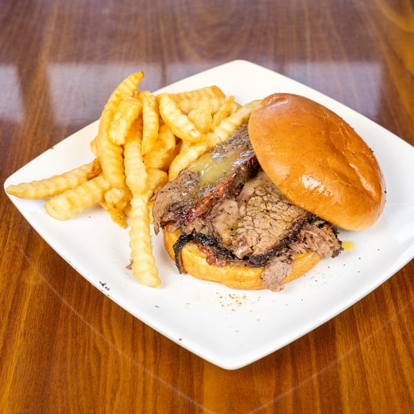 A southern brisket sandwich with gravy and crinkle-cut fries on a white plate at Melvin's at Riverside.