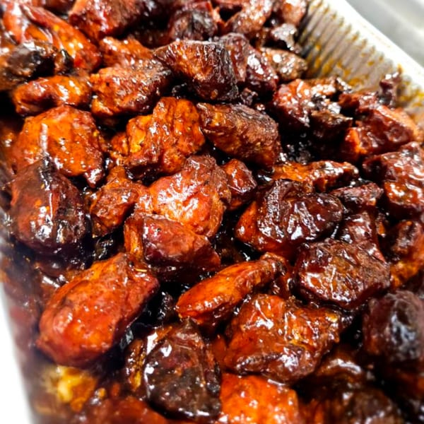 Close-up of glistening, dark brown and orange-red southern BBQ burnt ends in a metal tray.