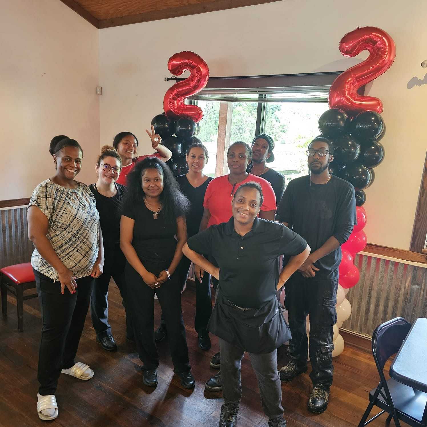 Group photo of nine people celebrating under 22 balloon decorations in a room.