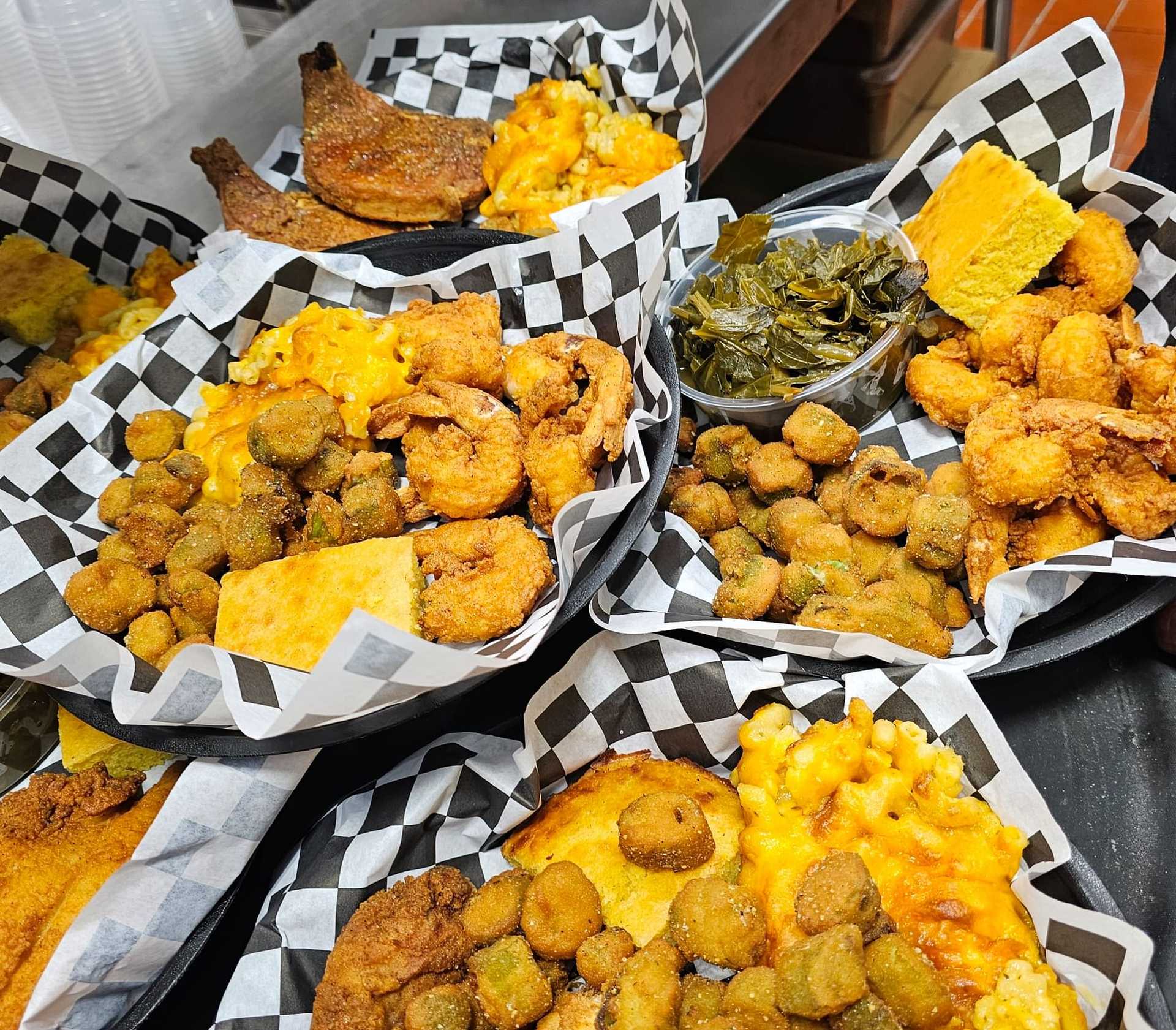 Baskets of fried food including shrimp, chicken, fried okra, mac and cheese, cornbread, and collard greens.