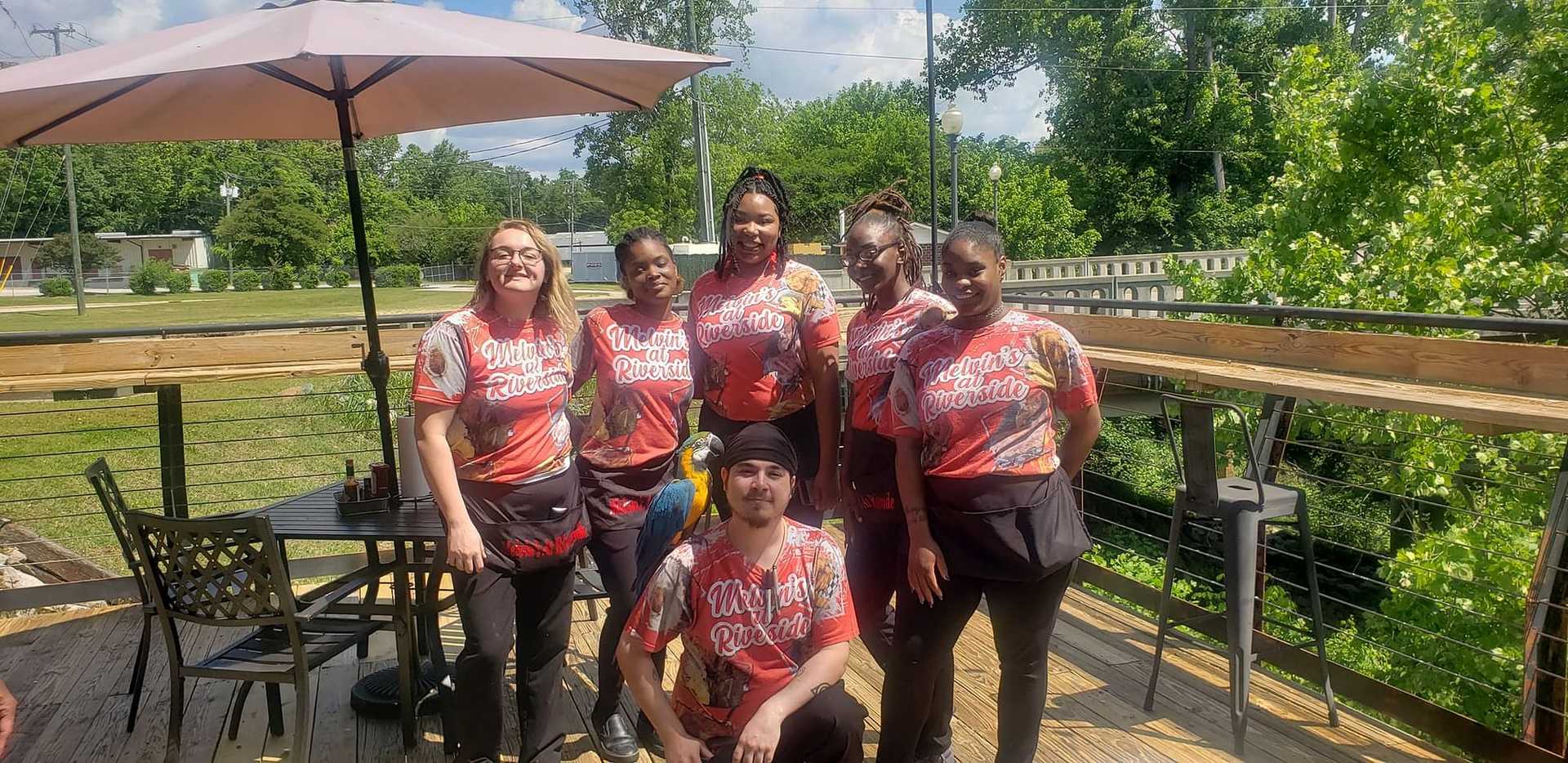 Outdoor portrait of six restaurant staff members in matching shirts, smiling at the camera.