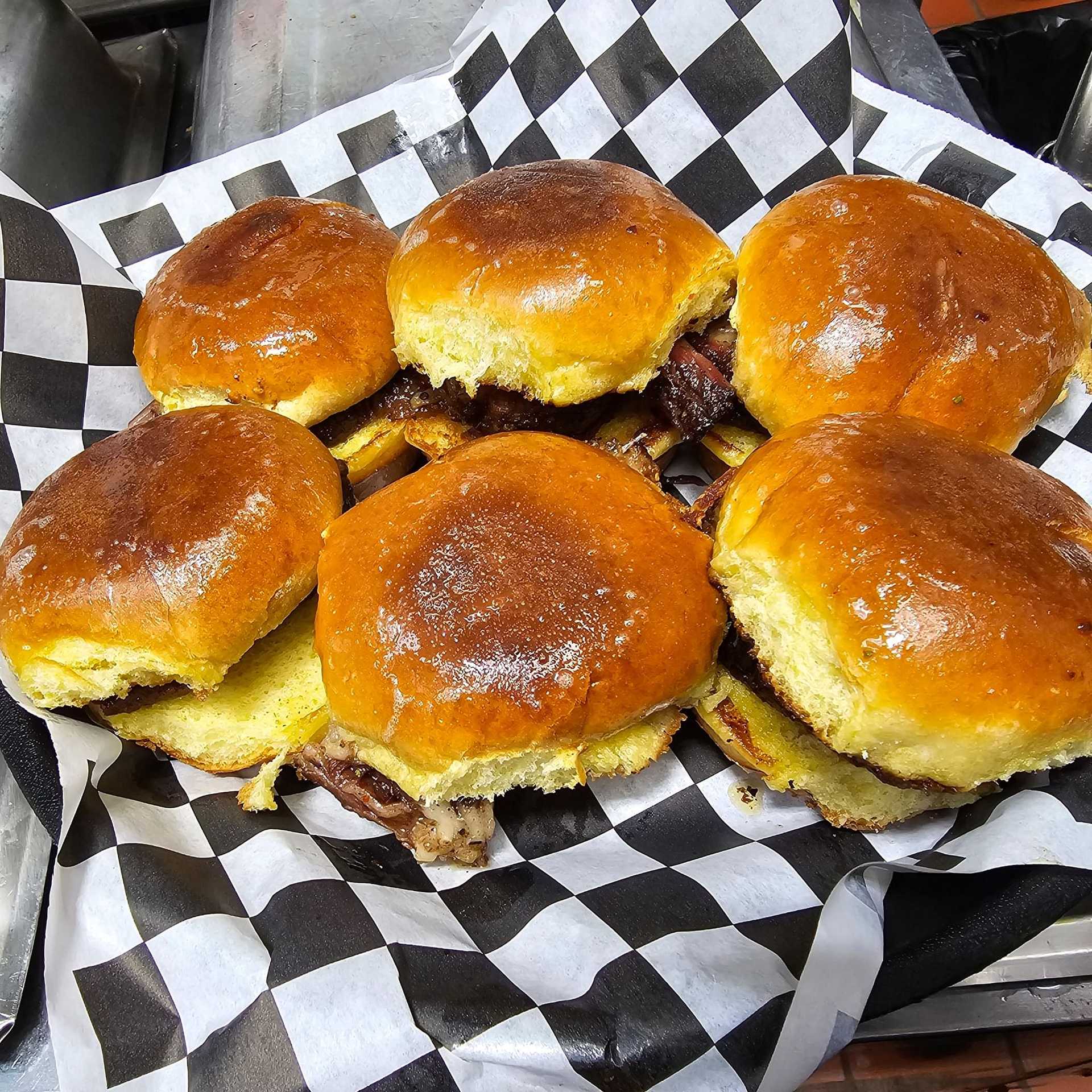 Six freshly grilled sliders on a checkered tray, showcasing toasted buns and juicy patties.